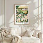 a framed poster of a garden with flowers hanging on a wall above a white couch with pillows.