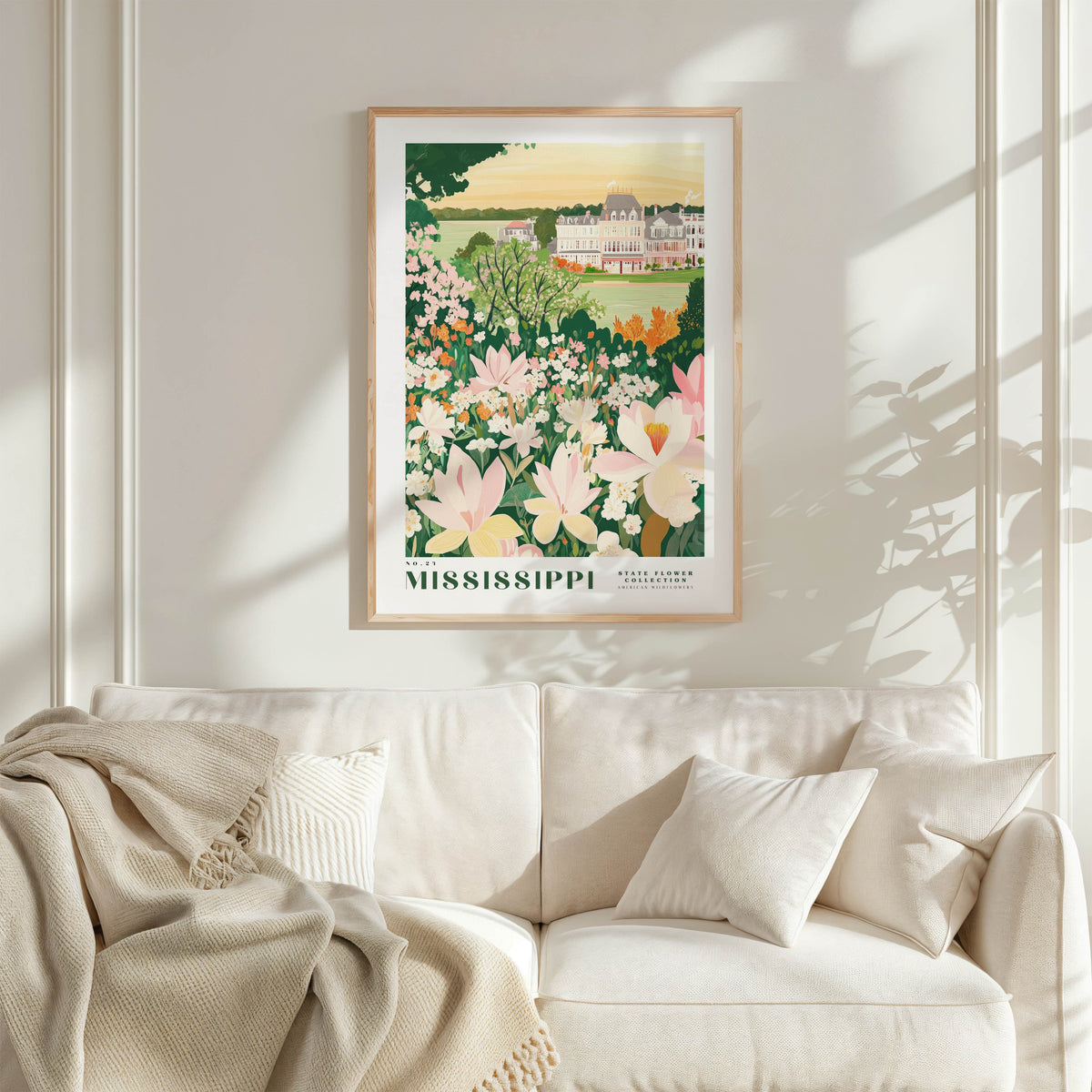 a framed poster of a garden with flowers hanging on a wall above a white couch with pillows.