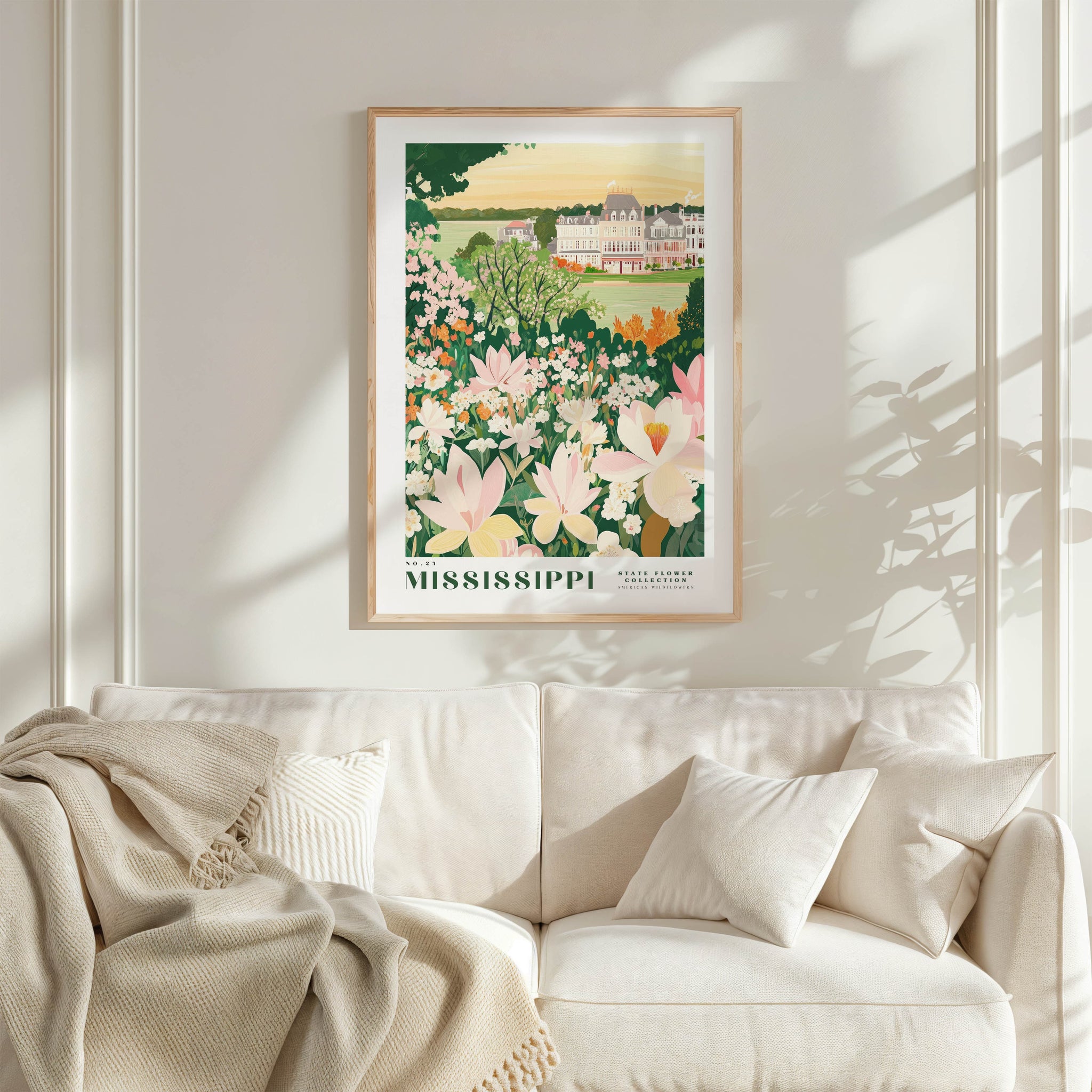 a framed poster of a garden with flowers hanging on a wall above a white couch with pillows.
