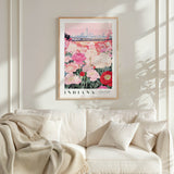 a framed poster of a cityscape with a field of flowers in the foreground, hanging on a wall above a white couch with a blanket draped over it.