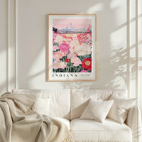 a framed poster of a cityscape with a field of flowers in the foreground, hanging on a wall above a white couch with a blanket draped over it.
