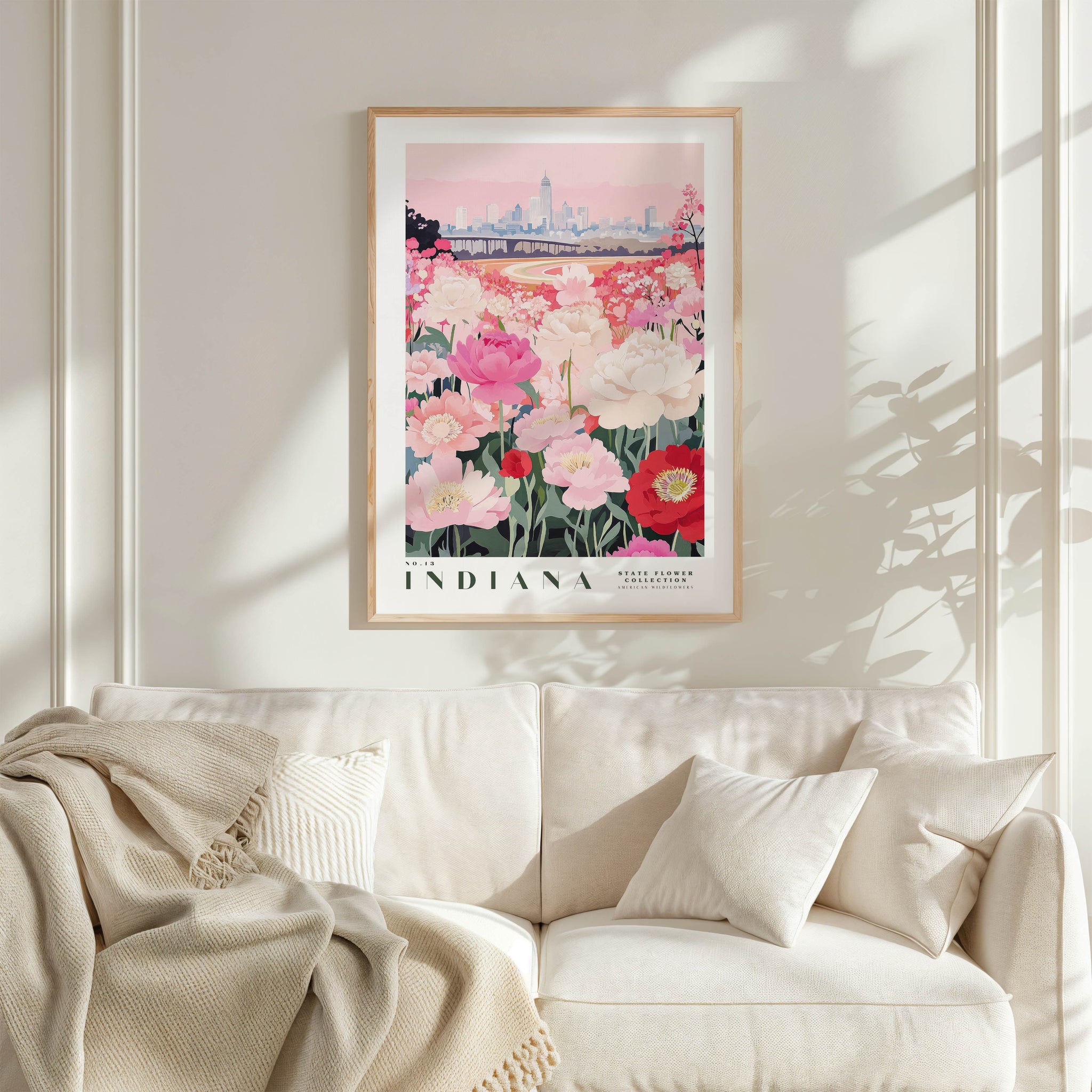 a framed poster of a cityscape with a field of flowers in the foreground, hanging on a wall above a white couch with a blanket draped over it.