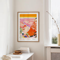 a framed poster of the Grand Canyon hanging on a wall, with a white table and a plant in the foreground.