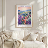 a framed poster of a colorful floral landscape hanging on a wall above a white couch with a blanket draped over it.