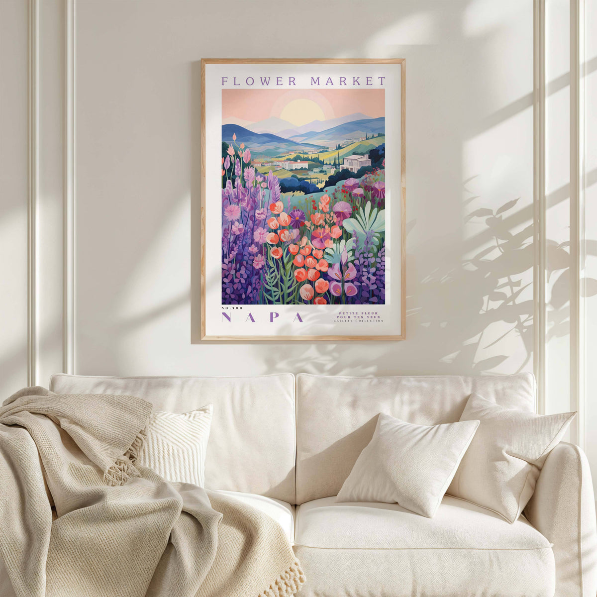 a framed poster of a colorful floral landscape hanging on a wall above a white couch with a blanket draped over it.