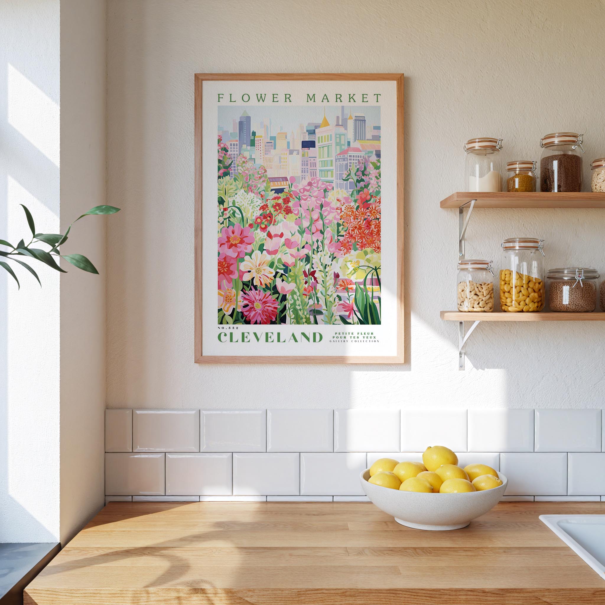a framed poster of a colorful floral scene hanging on a wall above a kitchen counter with a bowl of lemons on it.
