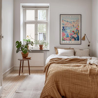 a cozy bedroom with a large bed, a wooden nightstand, and a window with a plant on the sill. The room has a warm, inviting atmosphere with a neutral color palette and natural elements like plants and a rug.