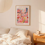 a bedroom scene with a framed poster of a flower market in Memphis hanging on the wall above a bed with striped pillows.