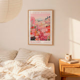 a bedroom scene with a framed poster of a flower market in Malibu hanging on the wall above a bed with striped pillows.