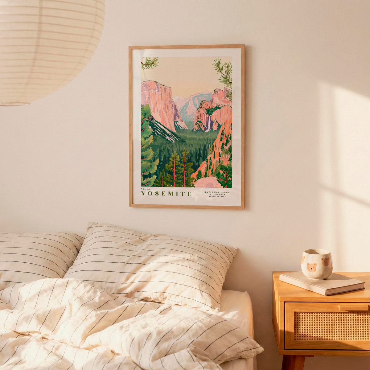 a framed poster of Yosemite National Park hanging on a wall above a bed with striped pillows.