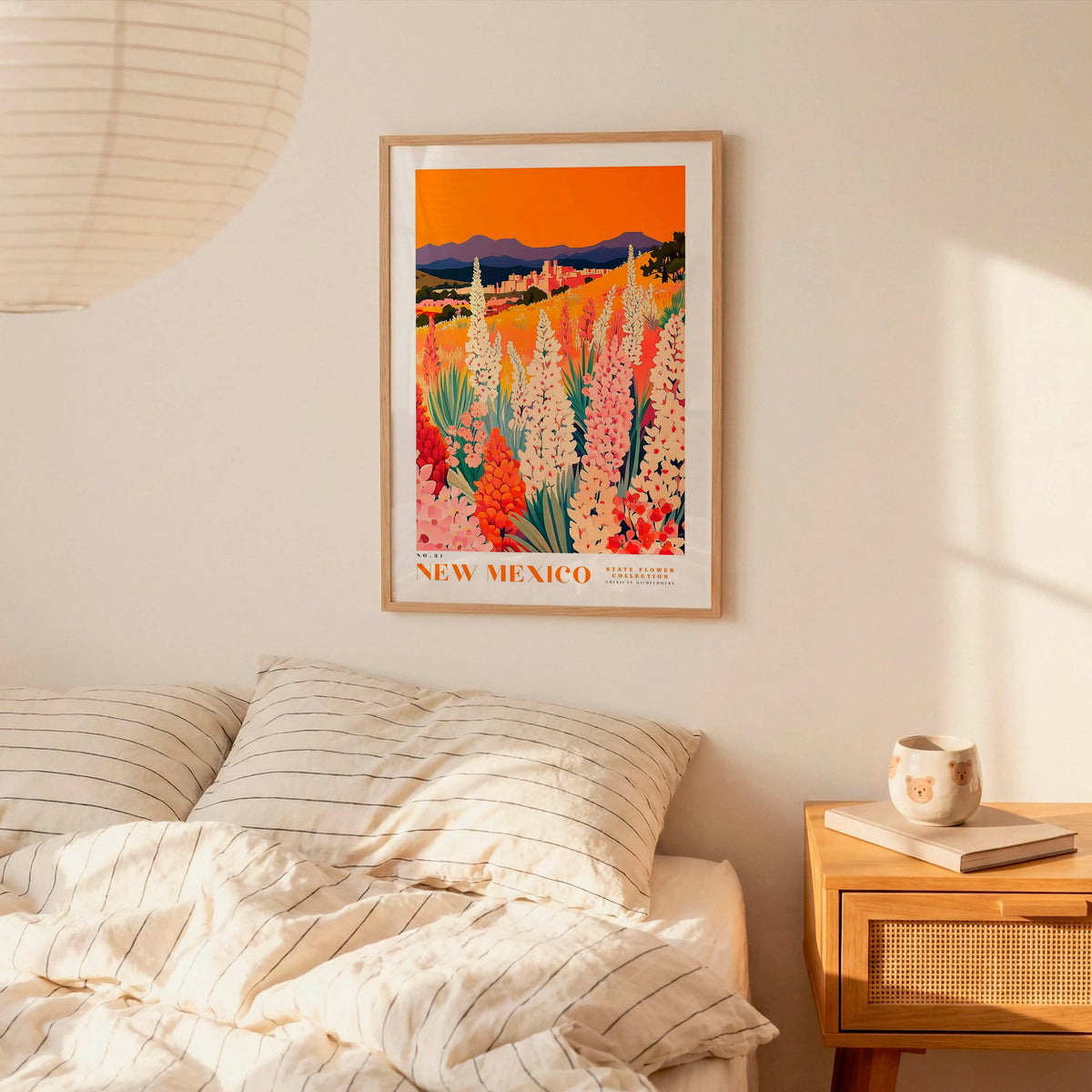 a bedroom scene with a framed poster of a colorful field of flowers hanging on the wall above a bed with striped pillows.