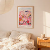 a bedroom scene with a framed poster of a flower market hanging on the wall above a bed with striped pillows.