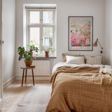 a cozy bedroom with a large bed, a wooden nightstand, and a window with a plant on the sill. The room has a warm, inviting atmosphere with a neutral color palette and natural elements like the potted plant and the rug.