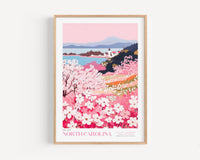 A framed poster depicting a scenic landscape with a lighthouse, mountains, and a field of blooming cherry blossoms.