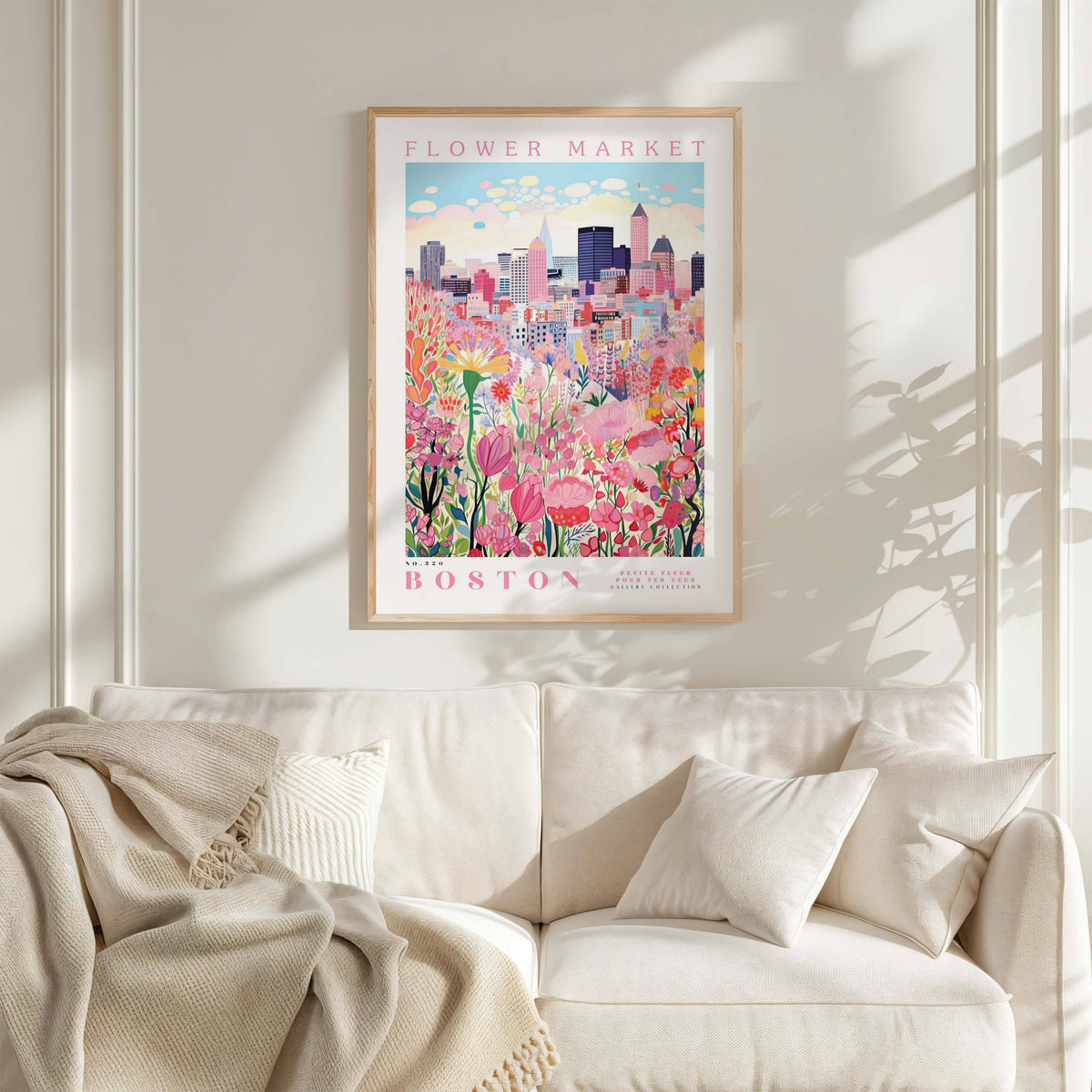 a framed poster of a cityscape with a flower market in the background, hanging on a wall above a white couch with a blanket draped over it.