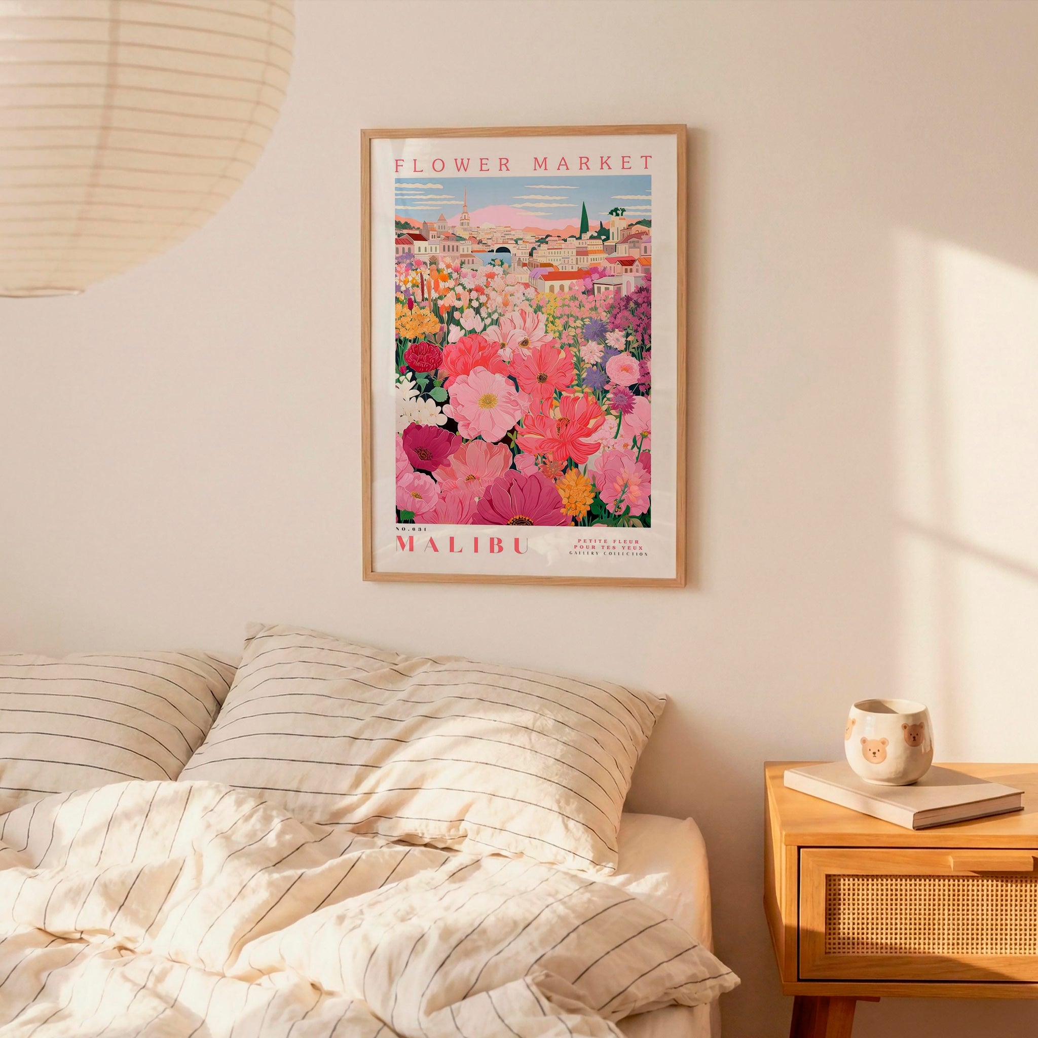 a framed poster of a colorful floral scene hanging on a wall above a bed with striped pillows.
