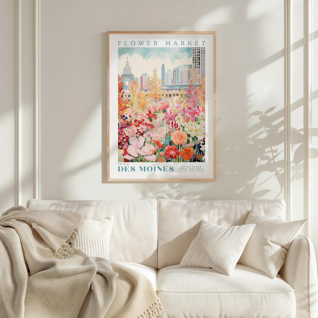 a framed poster of a colorful floral scene hanging on a wall above a white couch with a blanket draped over it.