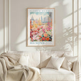 a framed poster of a colorful floral scene hanging on a wall above a white couch with a blanket draped over it.