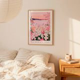 a bedroom scene with a framed poster of a floral landscape hanging on the wall above a bed with striped pillows.