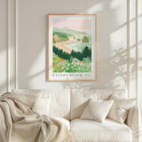 a framed poster of a scenic coastal landscape hanging on a wall above a white couch with a blanket draped over it.