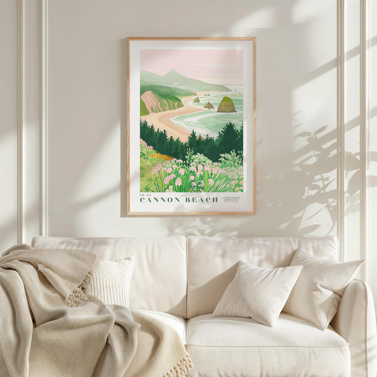 a framed poster of a scenic coastal landscape hanging on a wall above a white couch with a blanket draped over it.