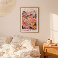 a framed poster of a colorful flower market in Cleveland, Ohio, hanging on a wall above a bed with striped pillows.