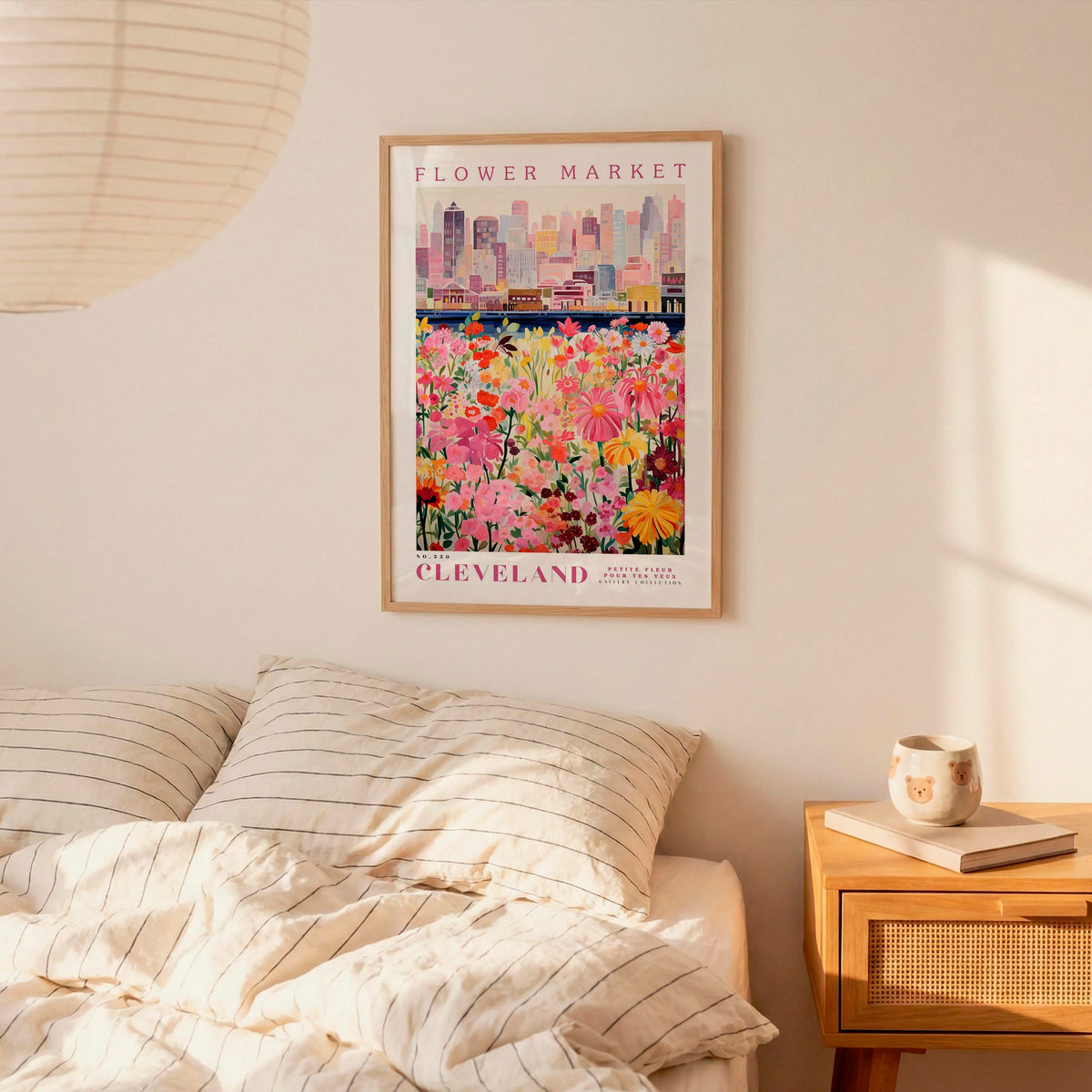 a framed poster of a colorful flower market in Cleveland, Ohio, hanging on a wall above a bed with striped pillows.
