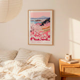 a bedroom scene with a framed poster of a floral landscape hanging on the wall above a bed with striped pillows.