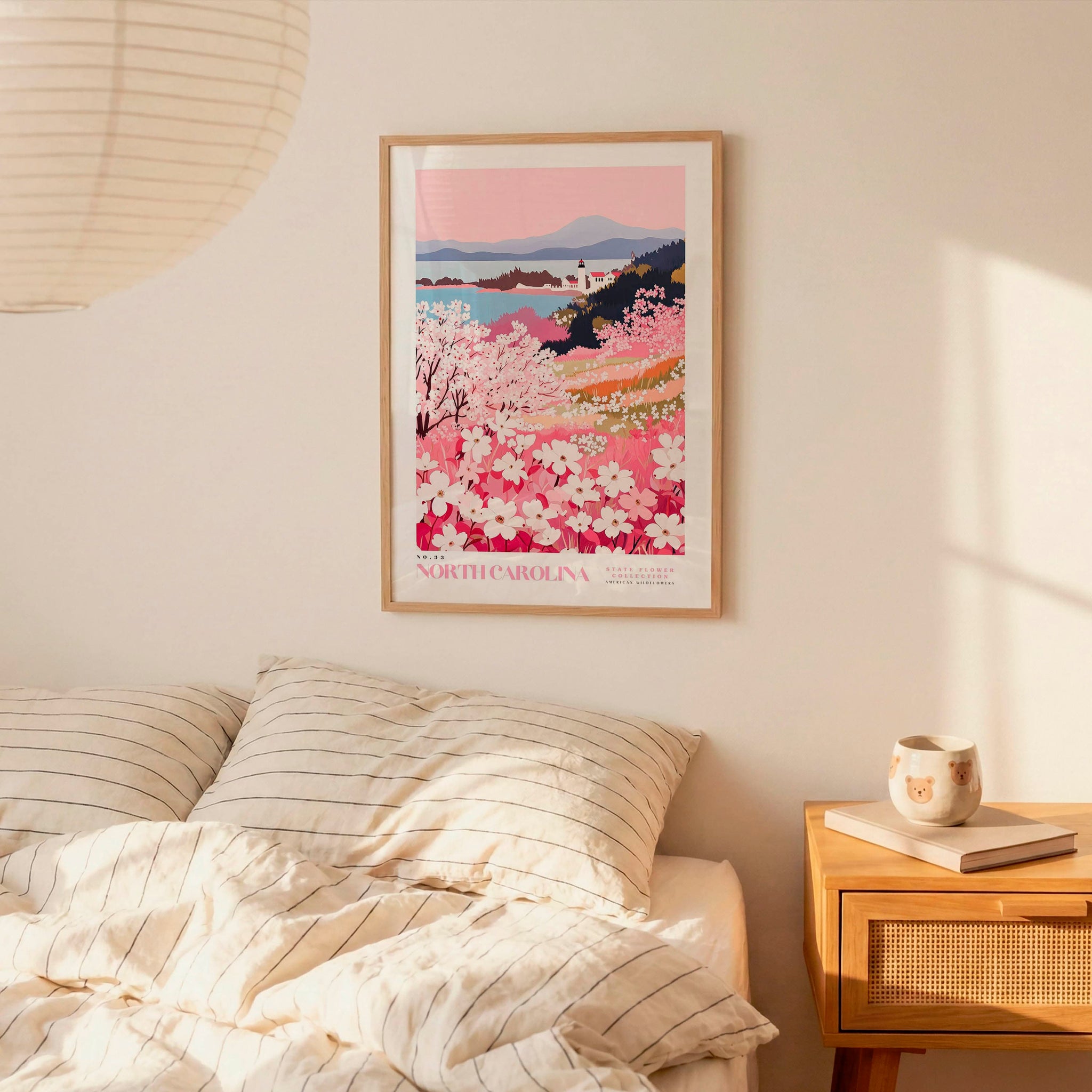 a bedroom scene with a framed poster of a floral landscape hanging on the wall above a bed with striped pillows.