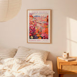 a bedroom scene with a framed poster of a colorful flower market hanging on the wall above a bed with striped pillows.