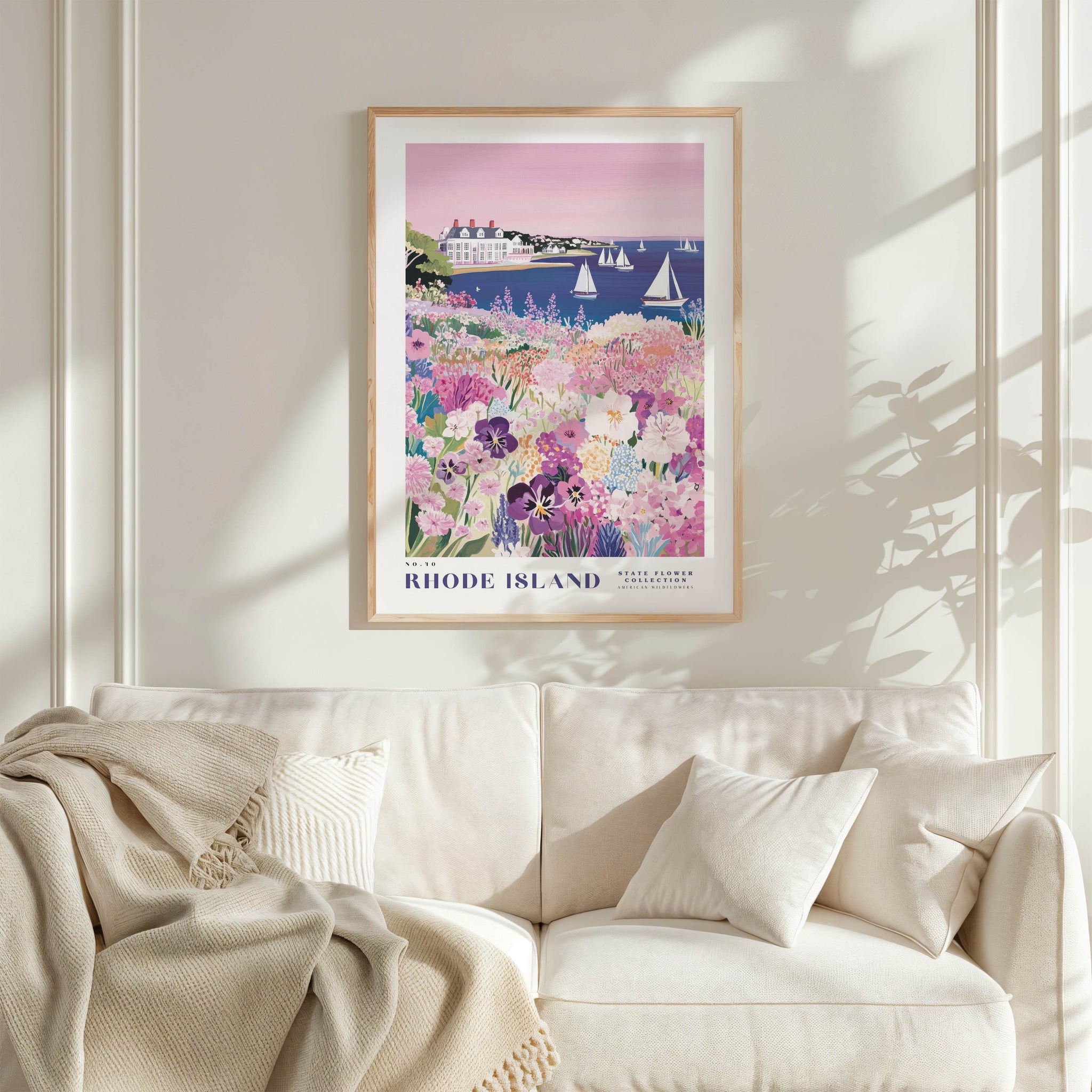 a framed poster of a scenic view of Rhode Island, with a lush garden and sailboats in the background. The poster is hung on a wall above a white couch, creating a cozy and inviting atmosphere in the living room.