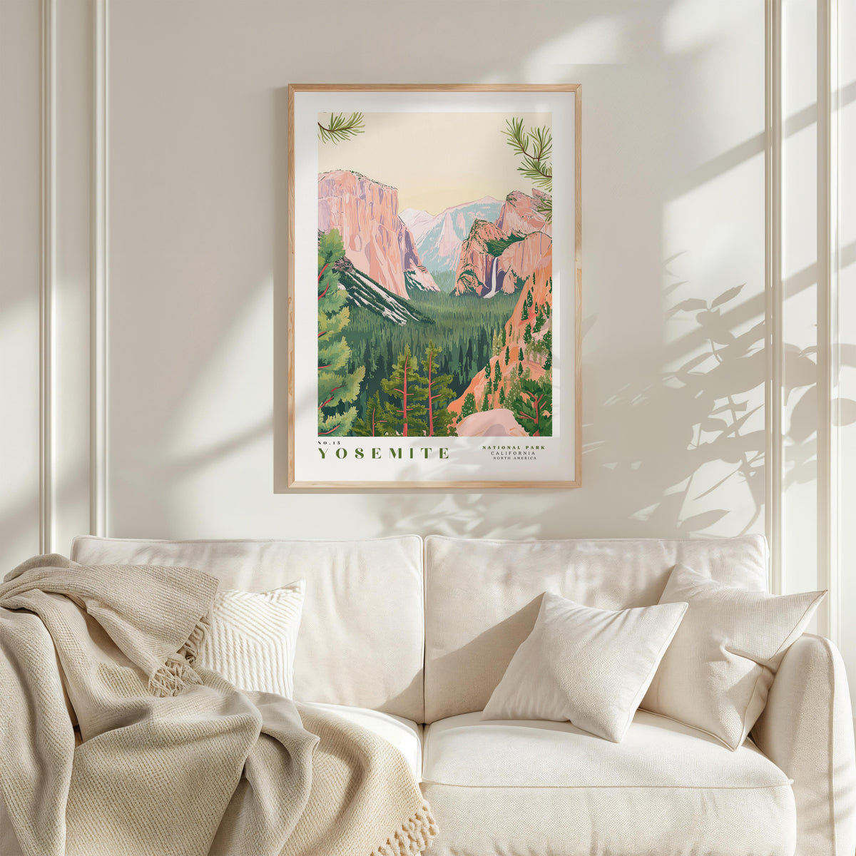 a framed poster of Yosemite National Park hanging on a wall above a white couch with a blanket draped over it.