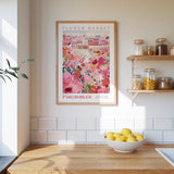 a kitchen scene with a framed poster of a colorful floral market in the background, a wooden counter with a bowl of lemons, and shelves displaying various jars and containers.