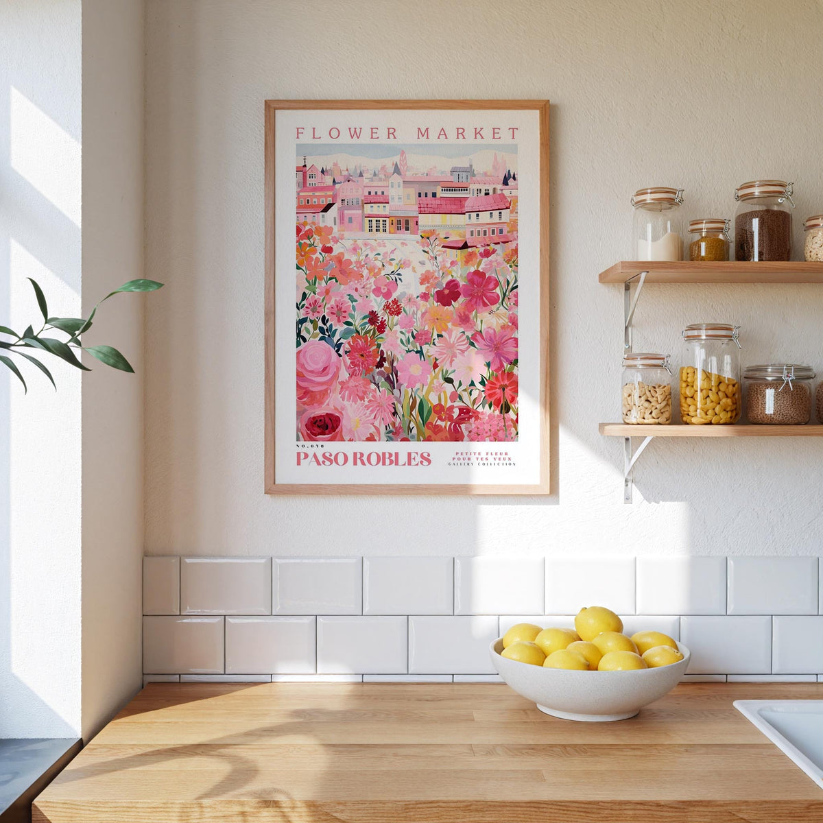 a kitchen scene with a framed poster of a colorful floral market in the background, a wooden counter with a bowl of lemons, and shelves displaying various jars and containers.