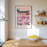a framed poster of a field of pink flowers hanging on a wall above a wooden countertop with a bowl of lemons.