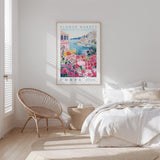 a bedroom with a large floral poster hanging on the wall, a woven chair, and a bed with white bedding.