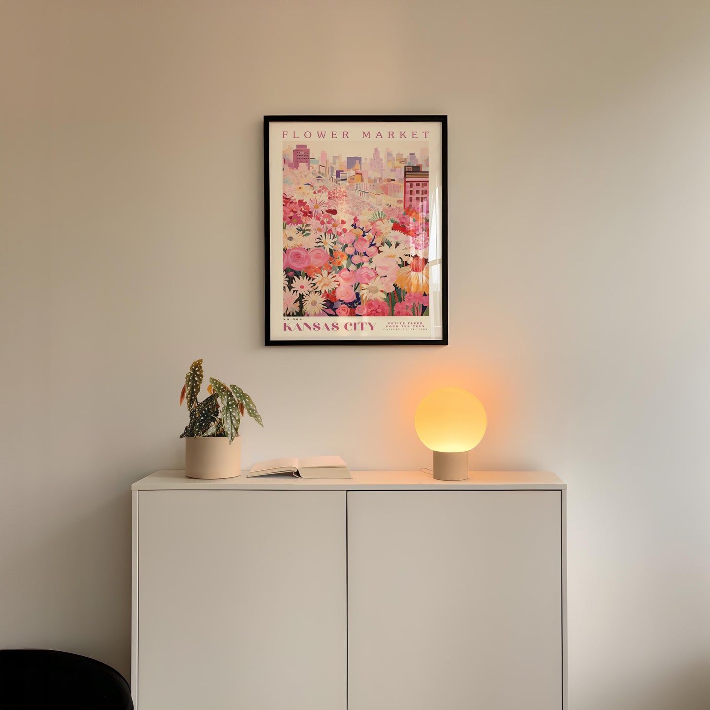 a white cabinet with a potted plant and a lamp on top, set against a wall with a framed poster of a cityscape above it.