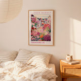 a bedroom scene with a framed poster of a colorful garden hanging on the wall above a bed with striped pillows.
