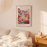 a bedroom scene with a framed poster of a colorful garden hanging on the wall above a bed with striped pillows.