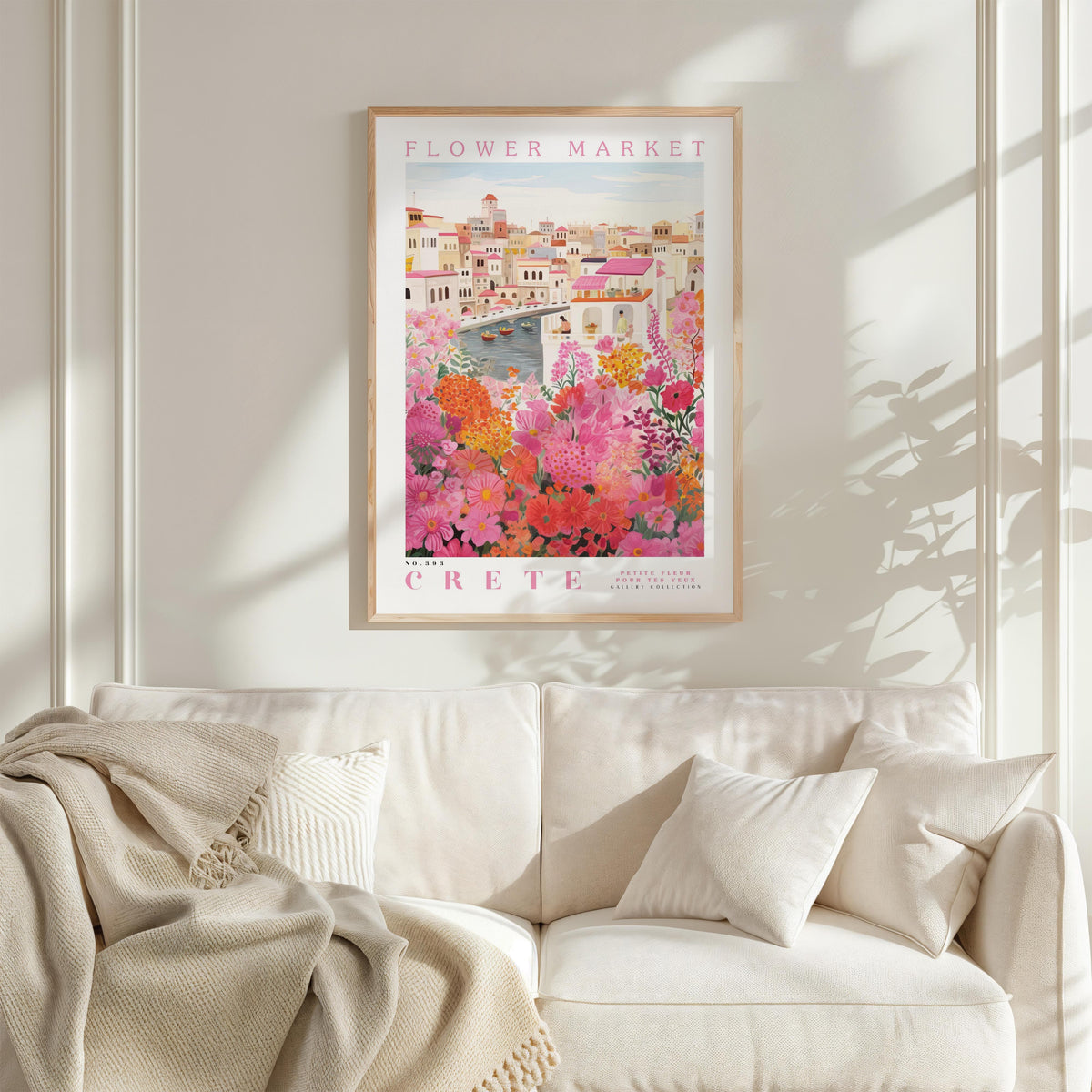 a framed poster of a colorful floral scene hanging on a wall above a white couch with a blanket draped over it.