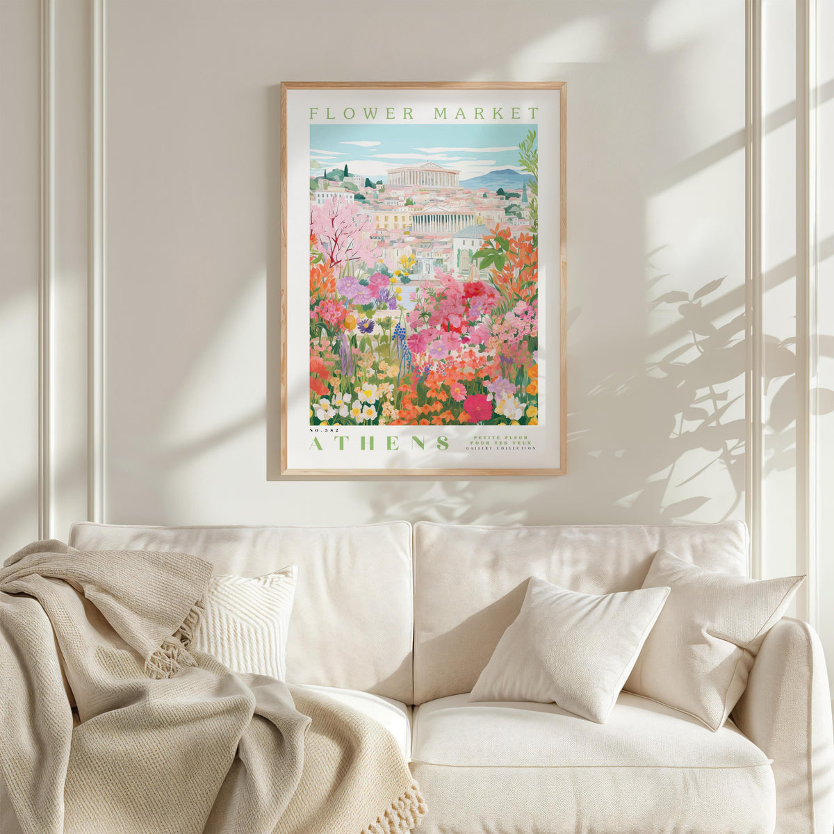 a framed poster of a colorful garden scene with flowers and buildings, hanging on a wall above a white couch.