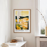 a framed poster of a scenic landscape with a steam vent in the background, hanging on a wall in a room with a window and a small table with books and a bowl on it.