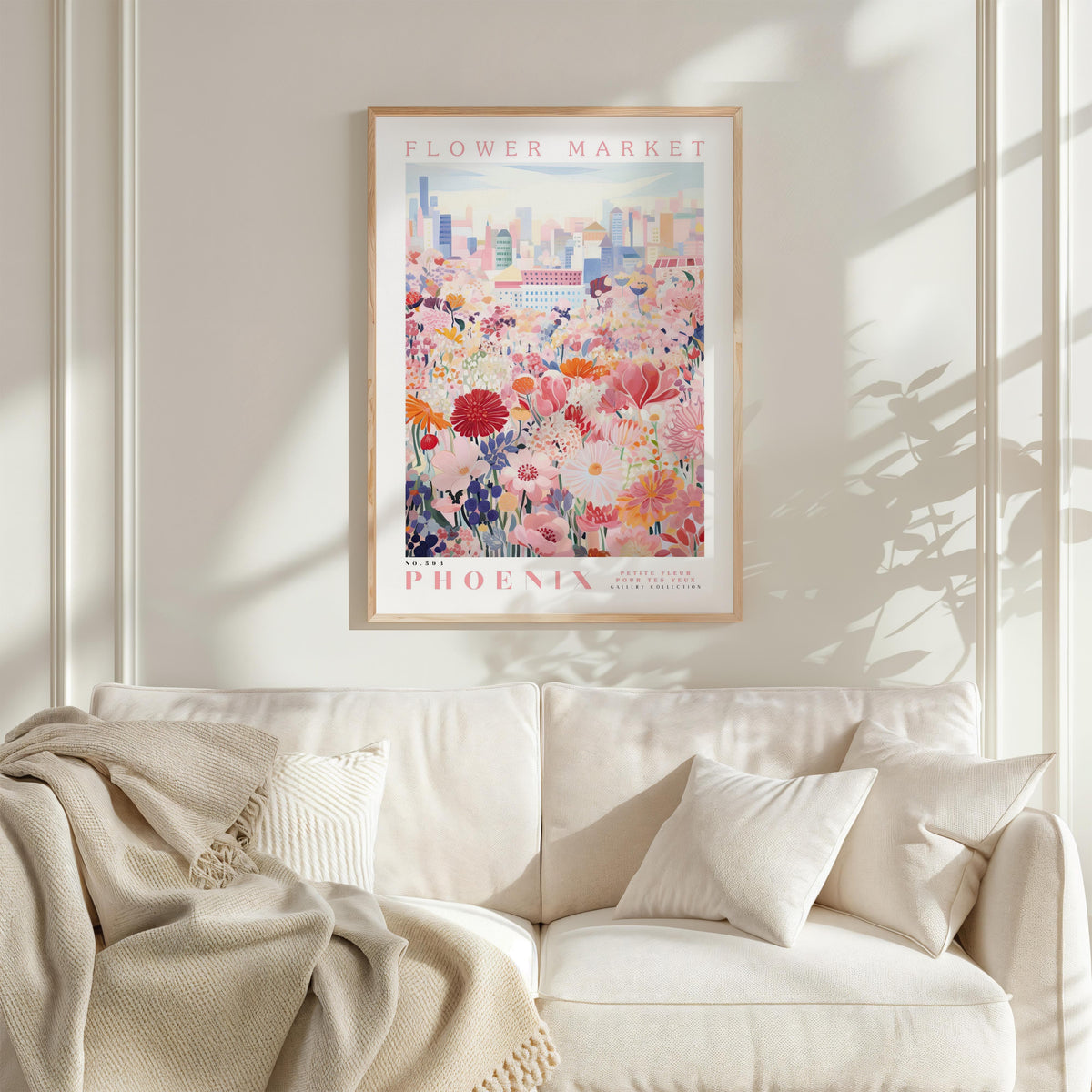 a framed poster of a cityscape with a field of flowers in the foreground, hanging on a wall above a white couch with a blanket draped over it.