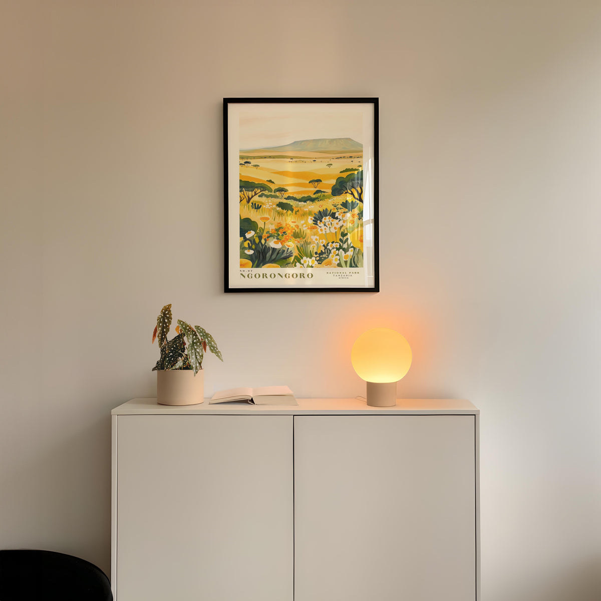 a white cabinet with a framed picture of a field hanging on the wall above it, and a small lamp on the cabinet.
