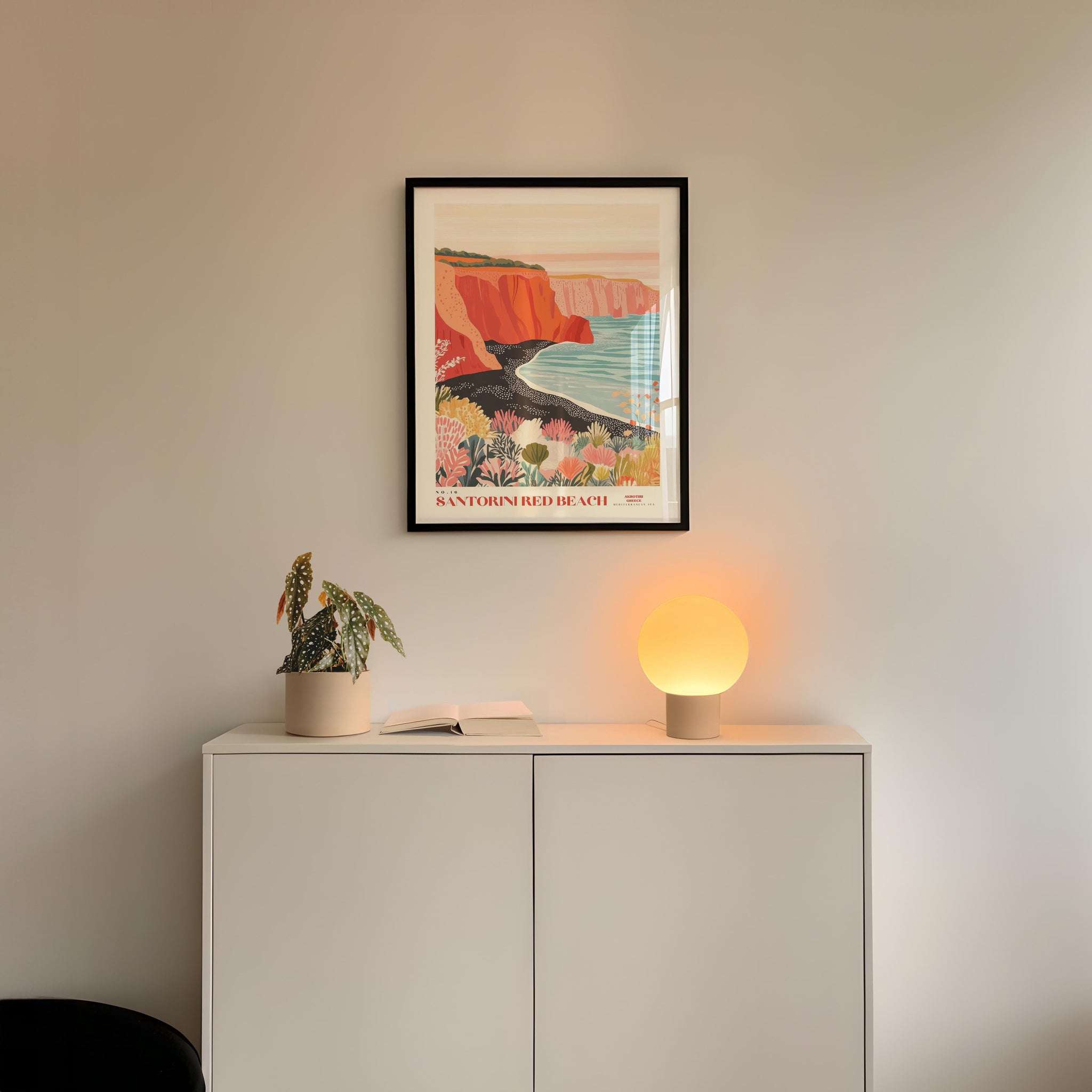 a white cabinet with a potted plant and a lamp on top, set against a white wall with a framed poster of a colorful landscape hanging above it.