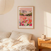 a framed poster of a cityscape with a field of flowers, hanging on a wall above a bed with striped pillows.