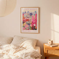 a bedroom setting with a framed poster of a colorful floral scene hanging on the wall above a bed with striped pillows.
