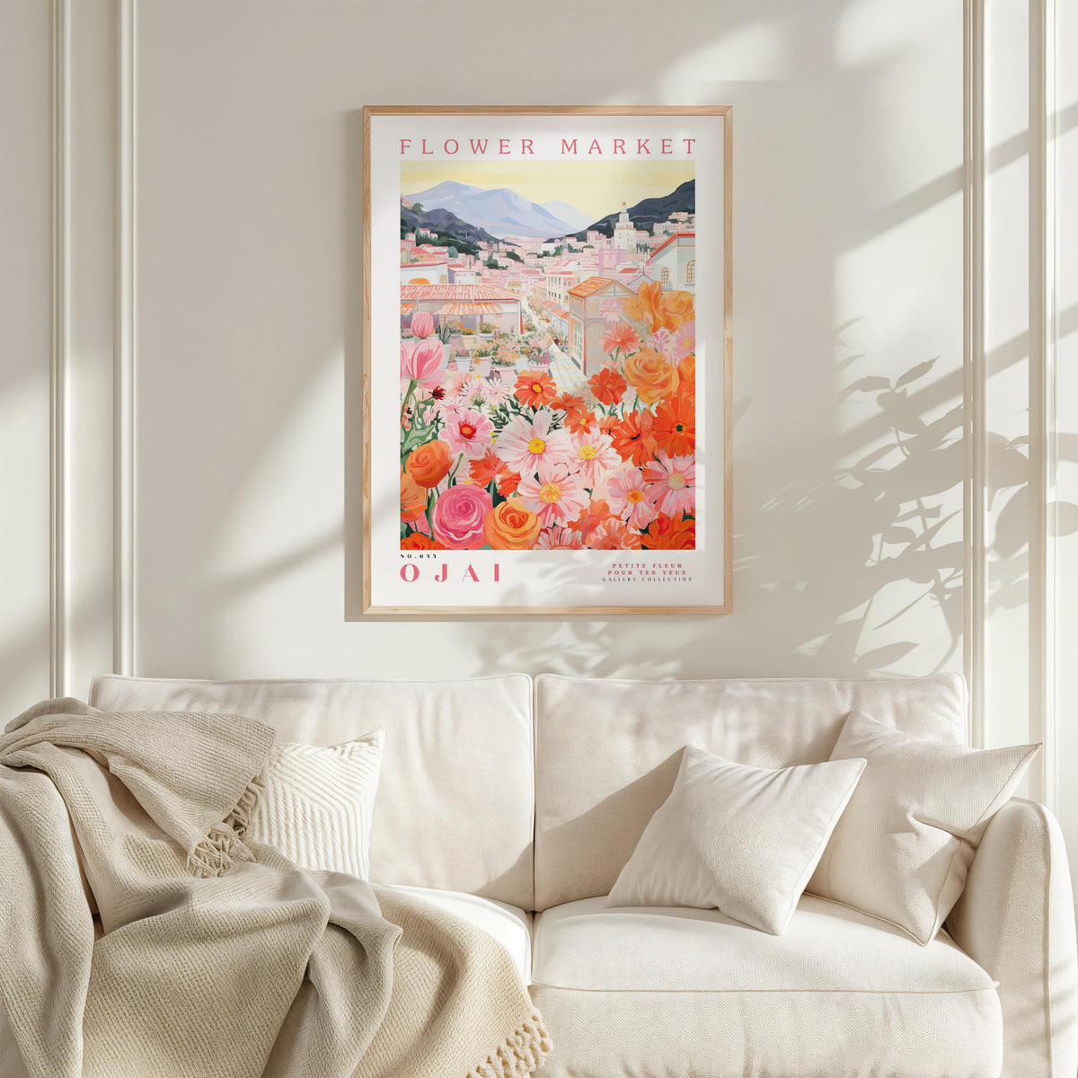 a framed poster of a colorful floral scene hanging on a wall above a white couch with a blanket draped over it.