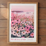 A framed poster depicting a scenic view of a field of pink flowers, with a body of water and boats in the background.