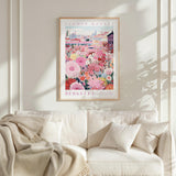a framed poster of a colorful floral scene hanging on a wall above a white couch with a blanket draped over it.